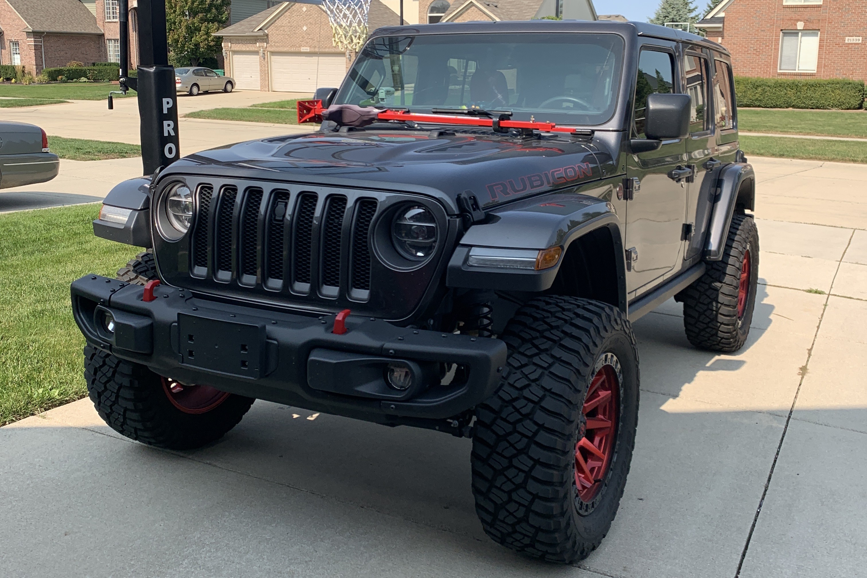 Front of the lifted Jeep Rubicon with red tow hooks and a red high-lift jack on the hood